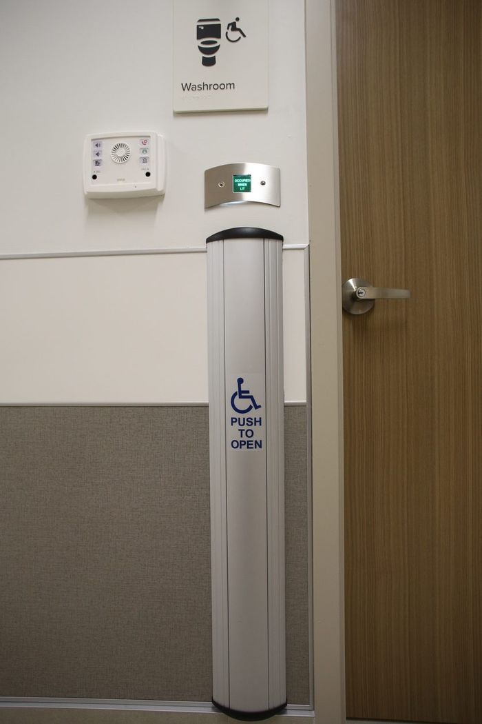 Push-to-open accessibility actuator beside an accessible washroom door
